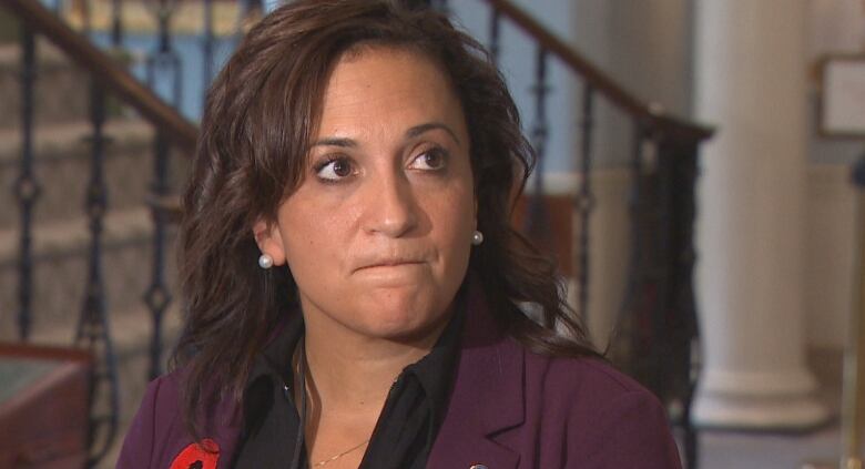 A woman with dark hair is wearing a maroon blazer with a poppy on the blazer