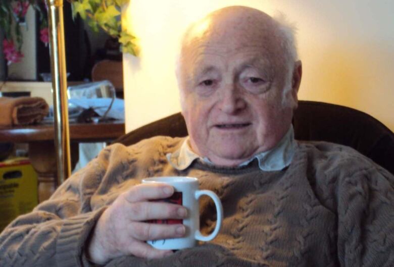 A man smiles while holding a mug.