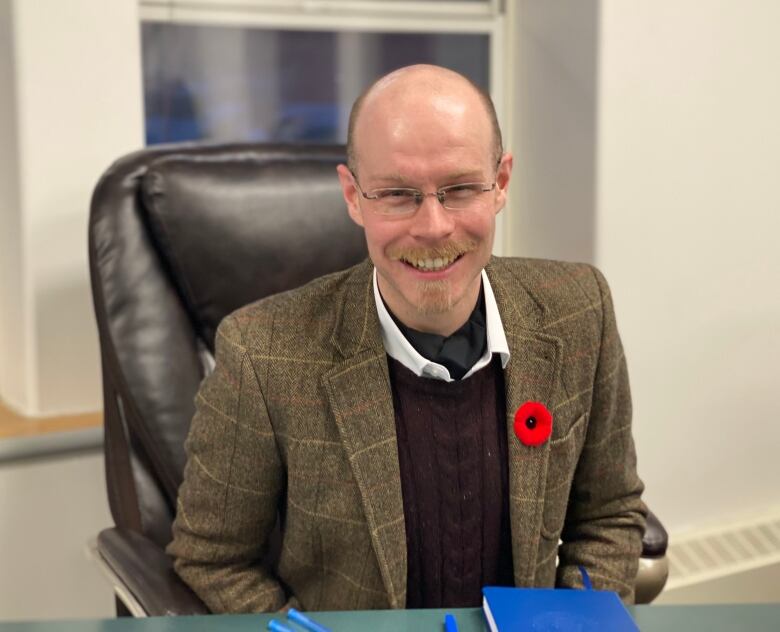 Man wearing glasses, a suit, and poppy smiling at the camera