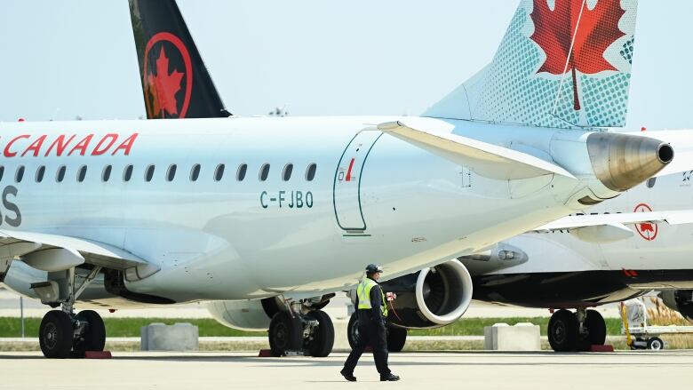 Two Air Canada jetliners sit on a runaway. A man walks in front of them. 