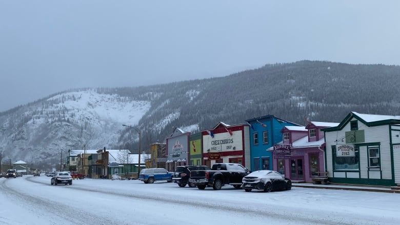 Colourful buildings line a snowy street. Behind them, a mountain rises.