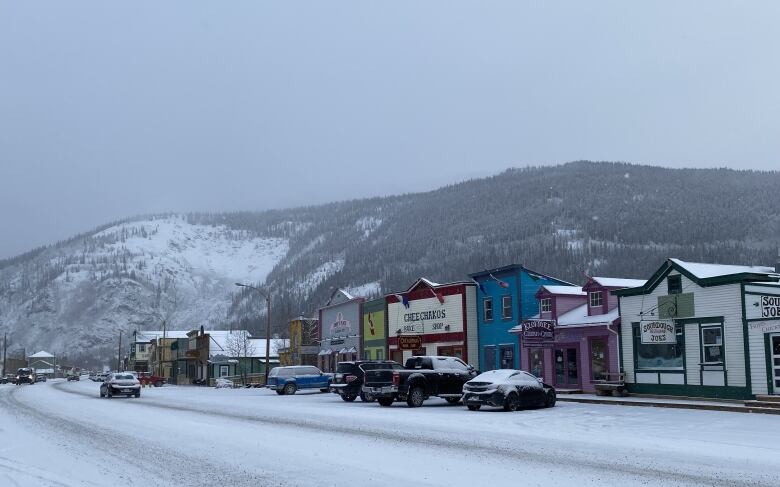 Colourful buildings line a snowy street. Behind them, a mountain rises.