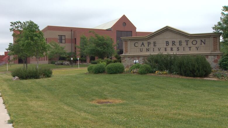 A red brick sign says Cape Breton University in front of a red brick building.