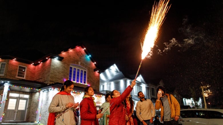 A group of people sets off fireworks in front of a home.