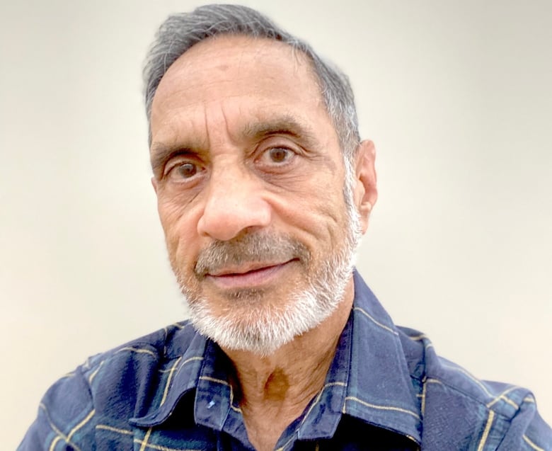 A man with grey hair and a grey beard wears a blue and yellow shirt.