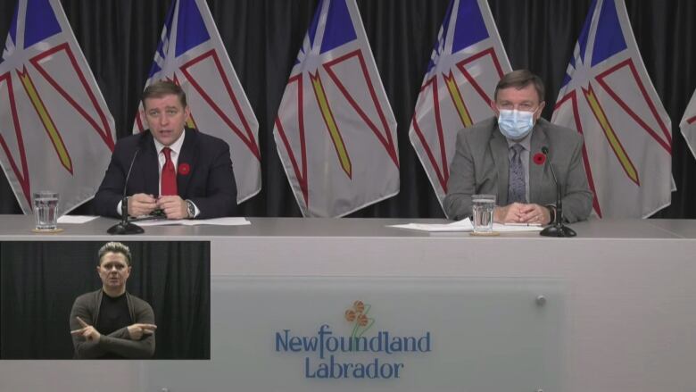 Two men are pictured at a podium, with flags behind them. One is wearning a mask. A sign language interpreter is shown in the bottom corner.