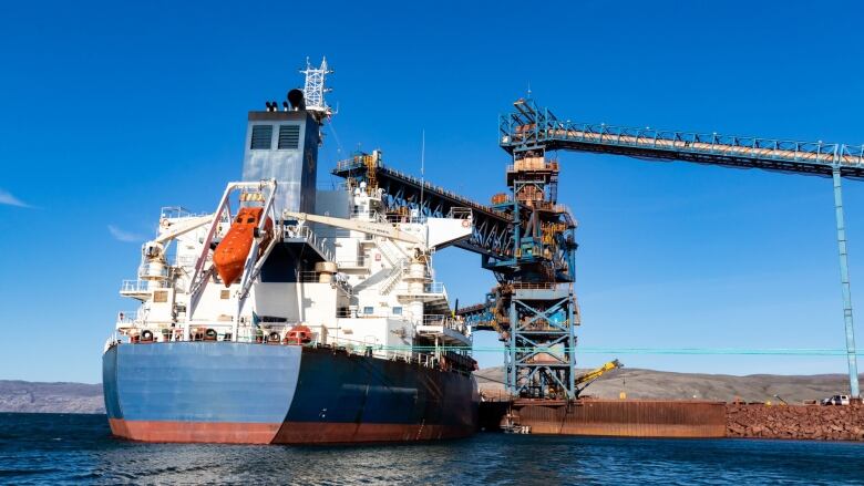 A large ship is seen at a dock and ore loader.