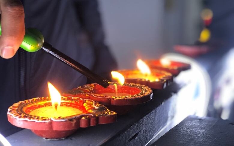 A hand lighting a row of small clay oil candles with a lighter.