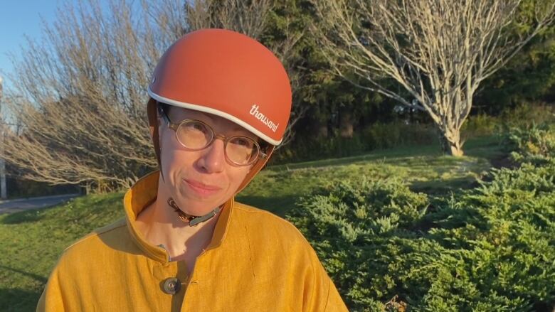 A woman in a yellow top wearing a bicycle helmet smiles at the camera.