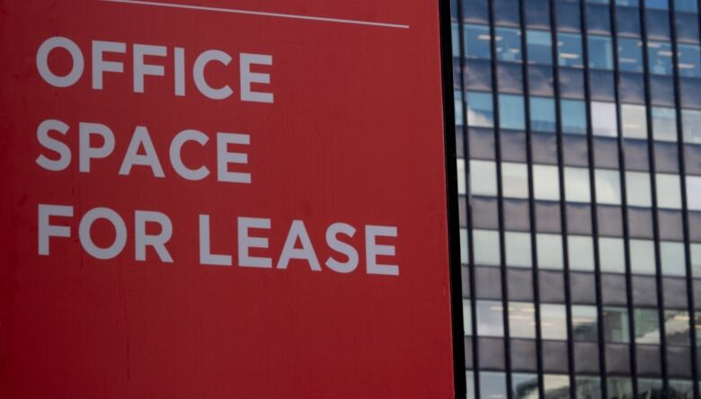 Red sign in front of glass office building. The sign reads 