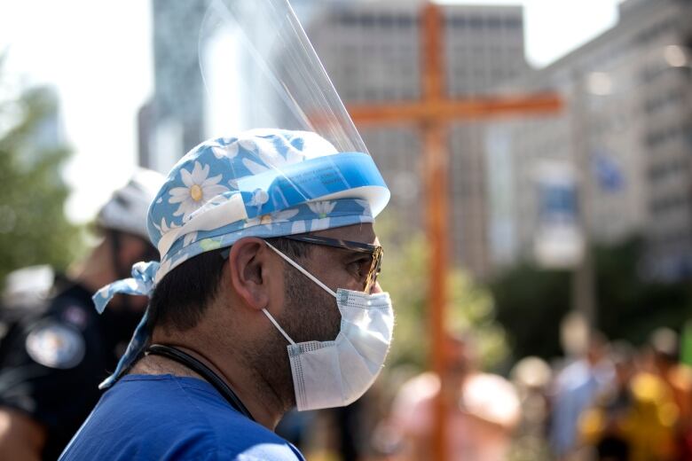 A healthcare professional watches as  demonstrators gather outside Toronto General Hospital, on September 13, 2021, to protest against COVID-19 vaccines, COVID-19 vaccine passports and COVID-19 related restrictions.