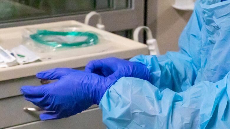 Arms and hands of someone wearing plastic blue hospital gown and blue protective gloves.