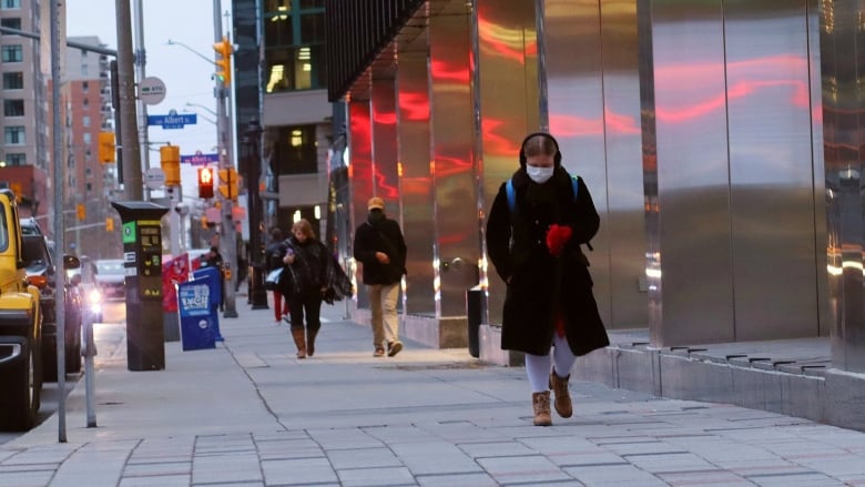 People walk along a city street at dusk in late autumn.