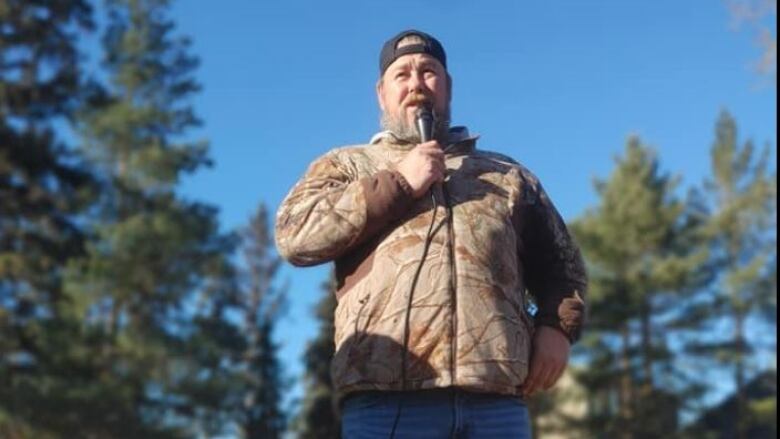 A man stands outside holding a microphone. 