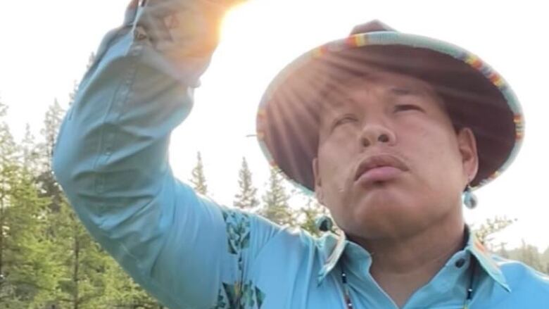 An Indigenous man in a blue shirt stands in the sun. 