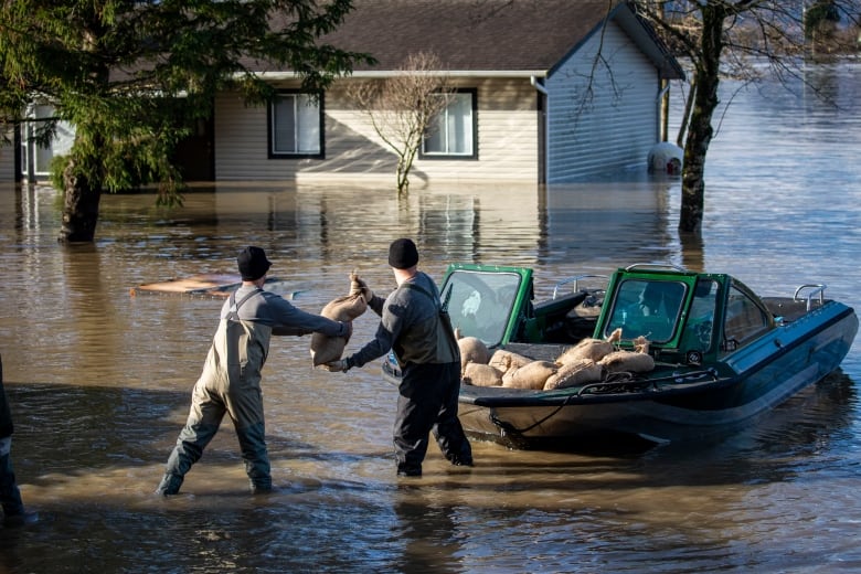 Two men load sandbags off a boat while standing in knee deep water 