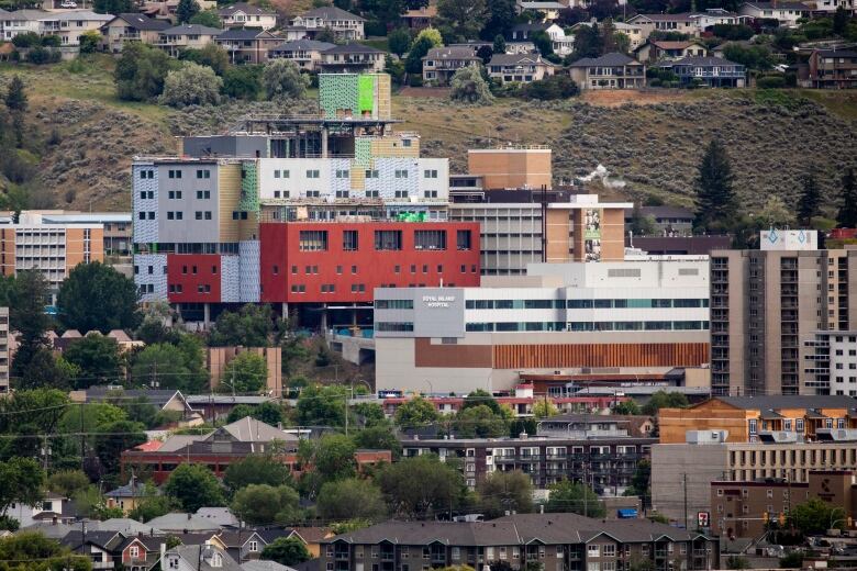 Royal Inland Hospital in Kamloops is shown in a long-distance photograph, standing in front of a scrubby hillside.