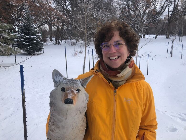 A woman smiles for a photo and poses with a fake coyote. 