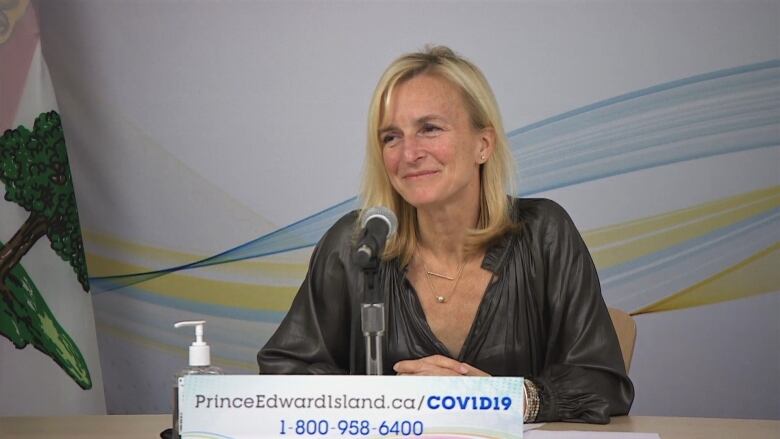 A blonde woman sits at a desk in front of a microphone and smiles.