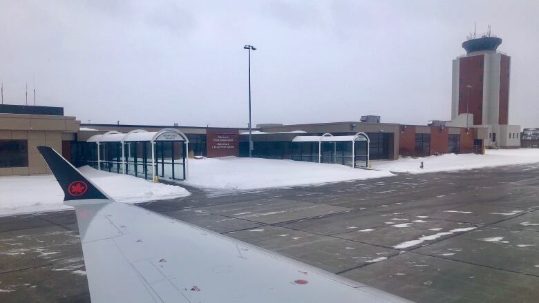 The wingtip of an Air Canada flight on the runway of Charlottetown Airport with the terminal and tower in the background. 