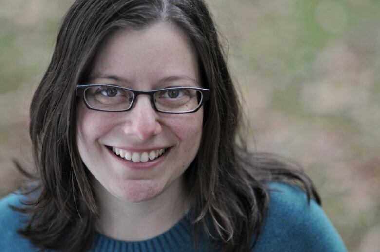 Smiling woman with shoulder-length brown hair and wearing glasses and a blue sweater.