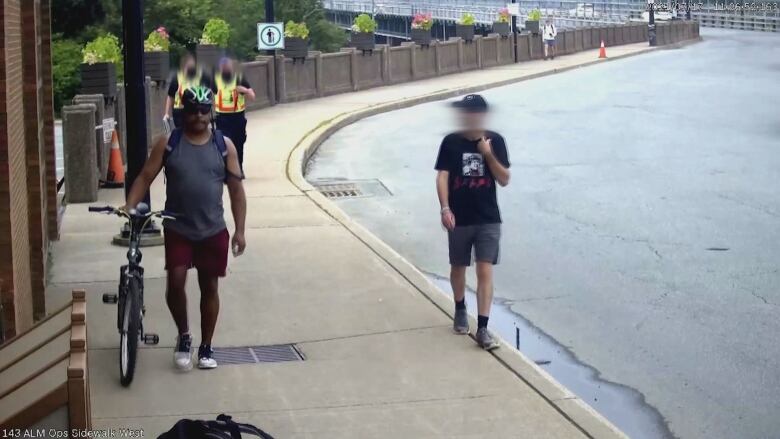 A photo taken from a surveillance video from Halifax Harbour Bridges shows Ross Gray walking his bike and being followed by officers in safety vests. 