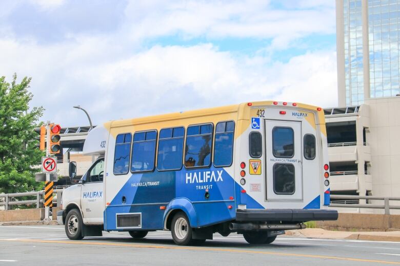 A blue, white and yellow bus with accessible symbols drives down a street