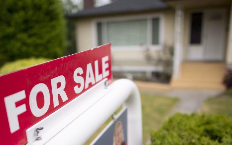 A real estate sign in front of a house that reads 'FOR SALE'.