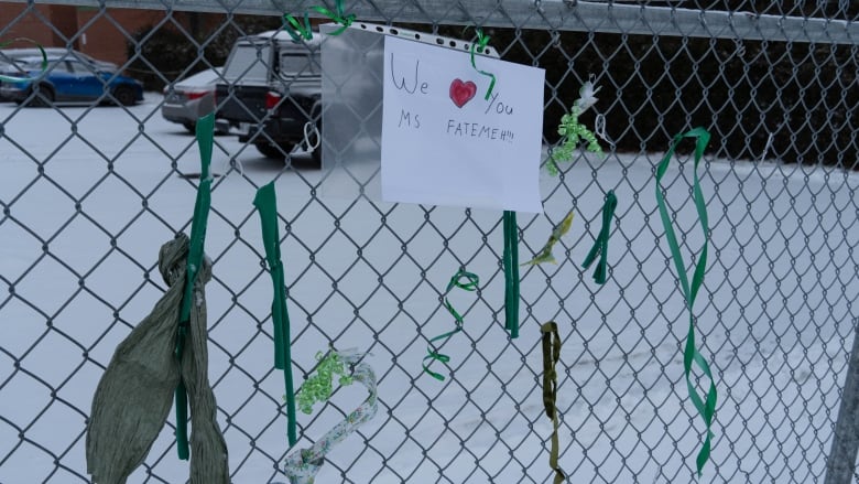 A hand drawn picture sits surrounded by green ribbons on the chain link fence outside Chelsea Elementary School says 