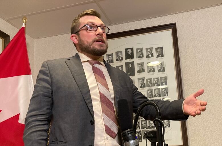 A man standing and speaking at a microphone which is placed at stomach-level. 