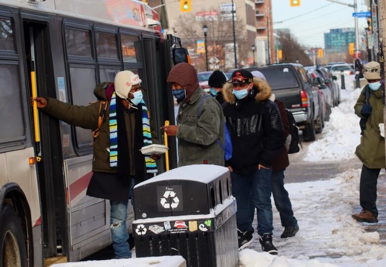 People wearing masks board a bus on a winter day.