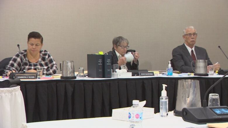 Three people sitting a a desk in front of mics