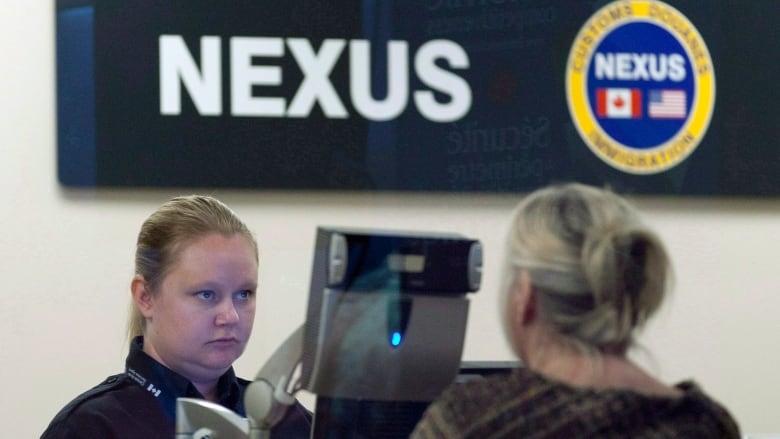 A woman border officer faces a woman passenger at an office in an airport.