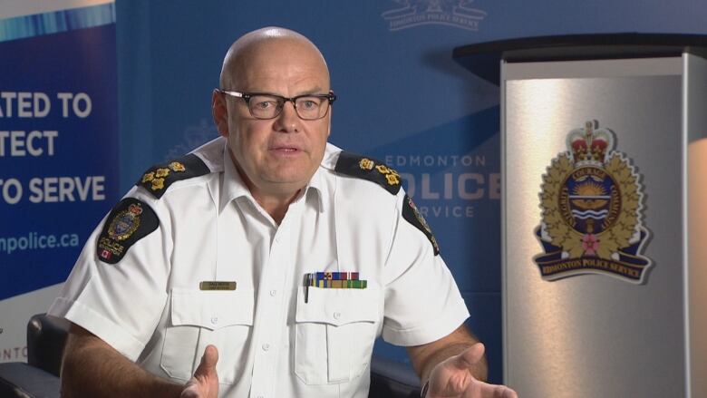 A man sits in a chair for an interview. He wears a white police uniform. 