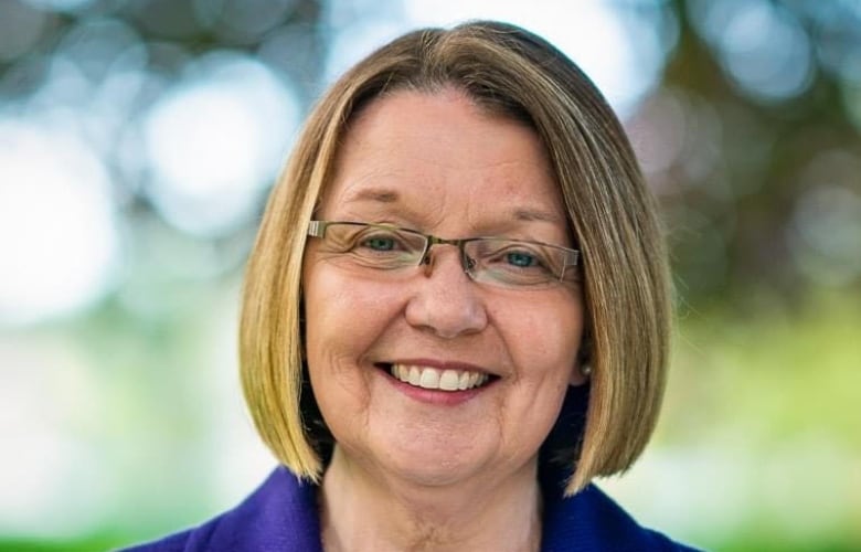 A smiling woman with short hair and glasses wearing a blue blazer. 