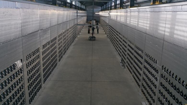 A picture inside a bitcoin mining facility shows long walls on either side of a concrete floor. The walls are filled with tiny computers.