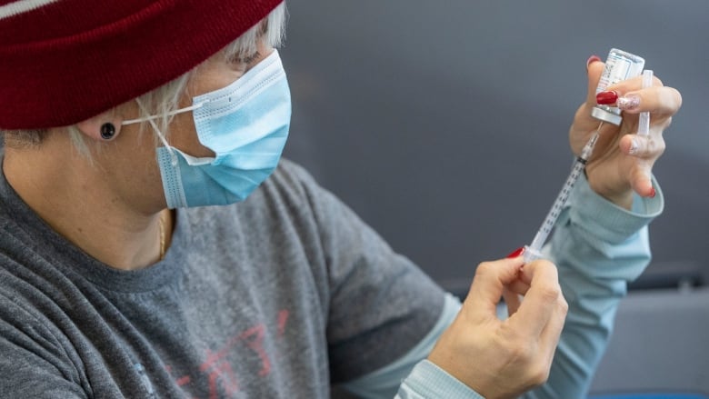 Someone puts a needle into a vial of vaccine at a clinic.