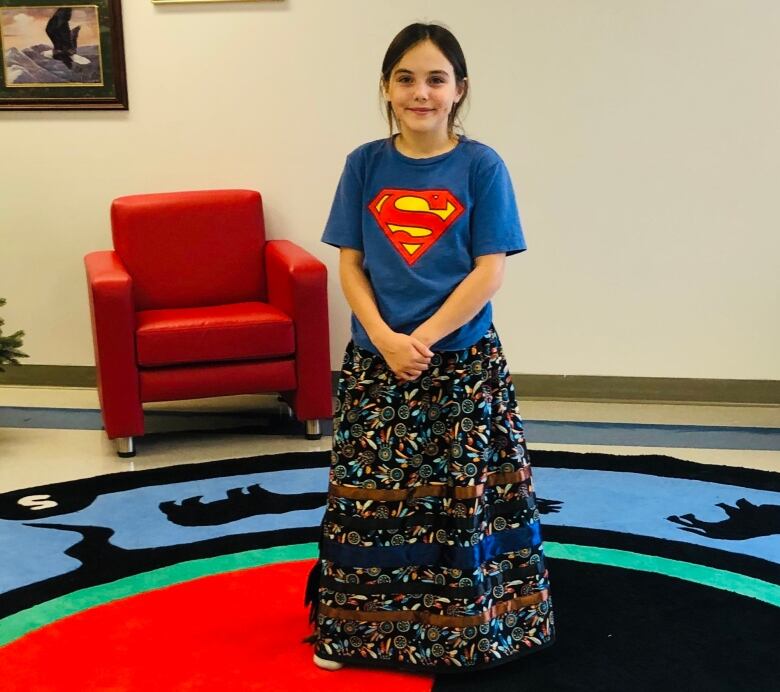 A young girl poses wearing a ribbon skirt.