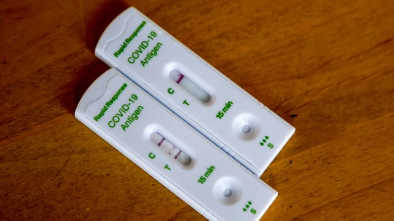 Two rapid COVID-19 tests, one with a positive result and the other with a negative result, are shown.