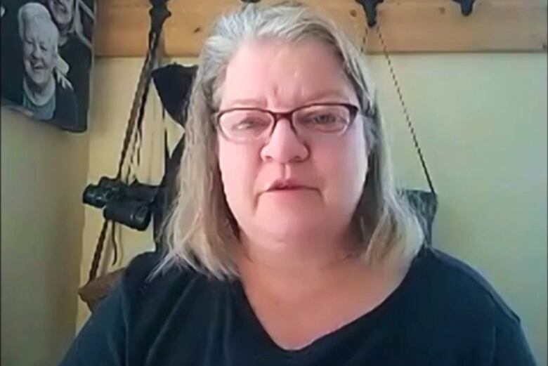 A woman with glasses and long, grey hair sits in a porch.