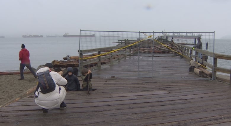 A fence blocks off access to a damaged pier on a stormy day.