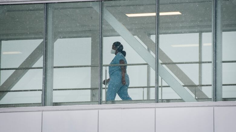 Hospital worker walks through a glass passageway.