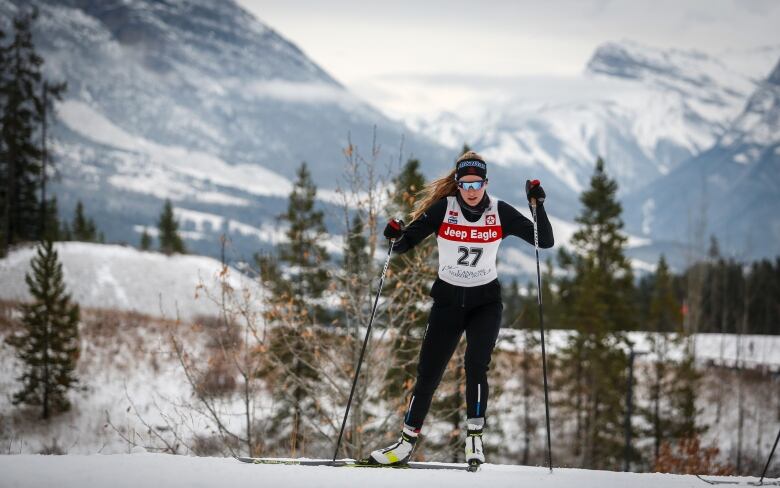 Dahria Beatty skiing in a race with a mountain and trees behind her.