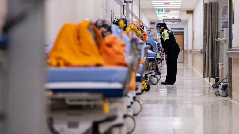 A hospital hallway is crowded with patients lying on stretchers as a paramedic checks on one of them.