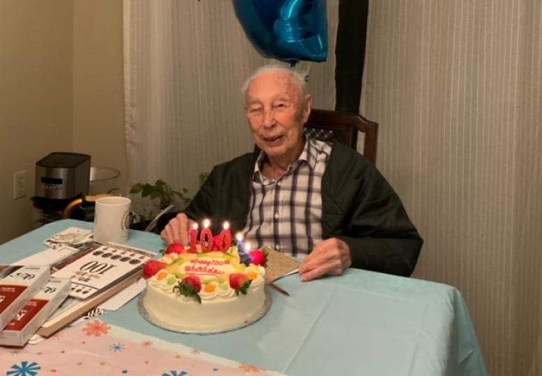 An older Japanese man smiles as he sits in front of a cake with '100' candle on it.