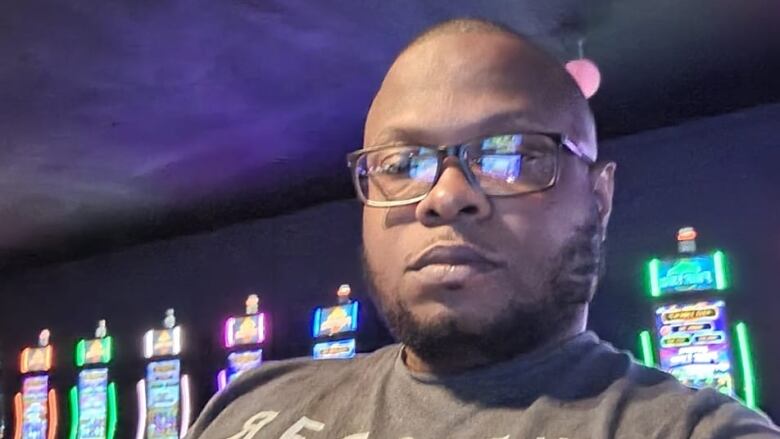 A man with a beard and glasses looks at the camera with what appears to be VLT machines in the background.