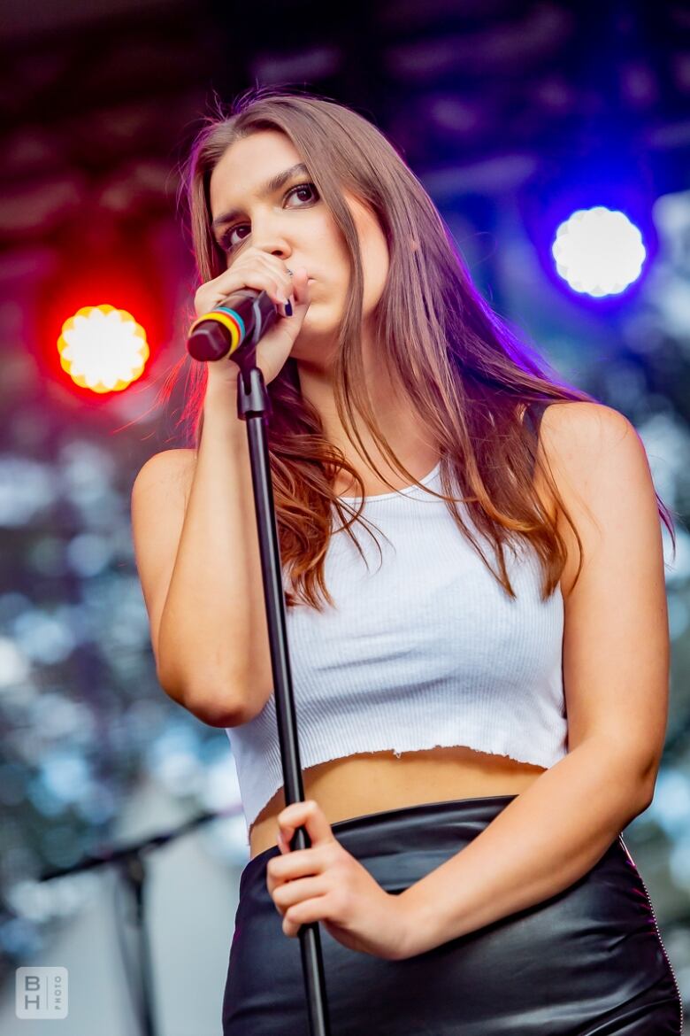 A white woman sings on a mic onstage in front of an orange and blue light