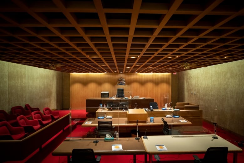 A courtroom interior with a crest of British Columbia behind a judge's desk. Various desks and benches sit in front of the judge's station.