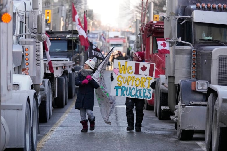 Two people walk between rows of trucks. One holds a flag and another holds a sign saying 