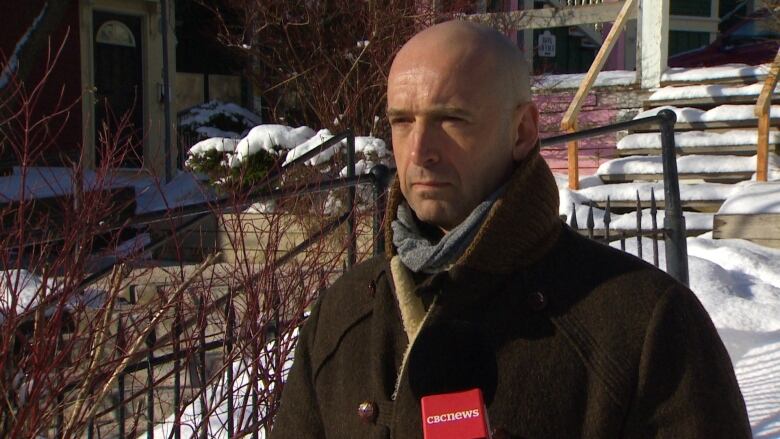 Man stands outside in winter setting, speaking into CBC microphone.